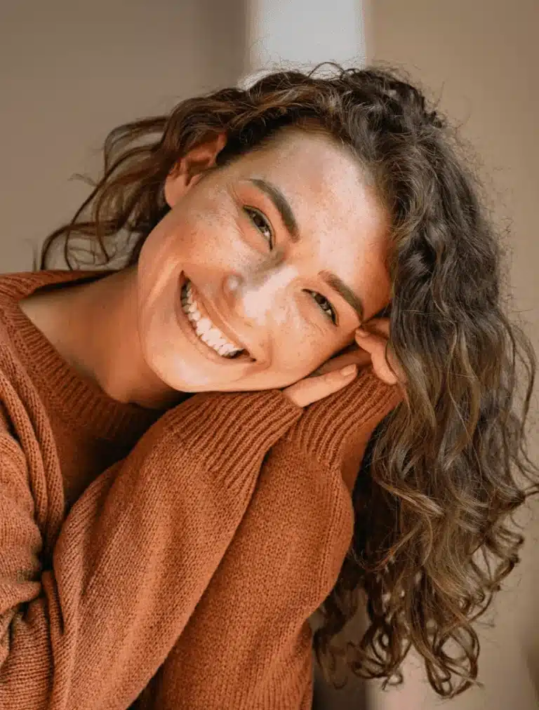 Close-up of a cheerful woman in a red sweater leaning on her hand and smiling warmly.