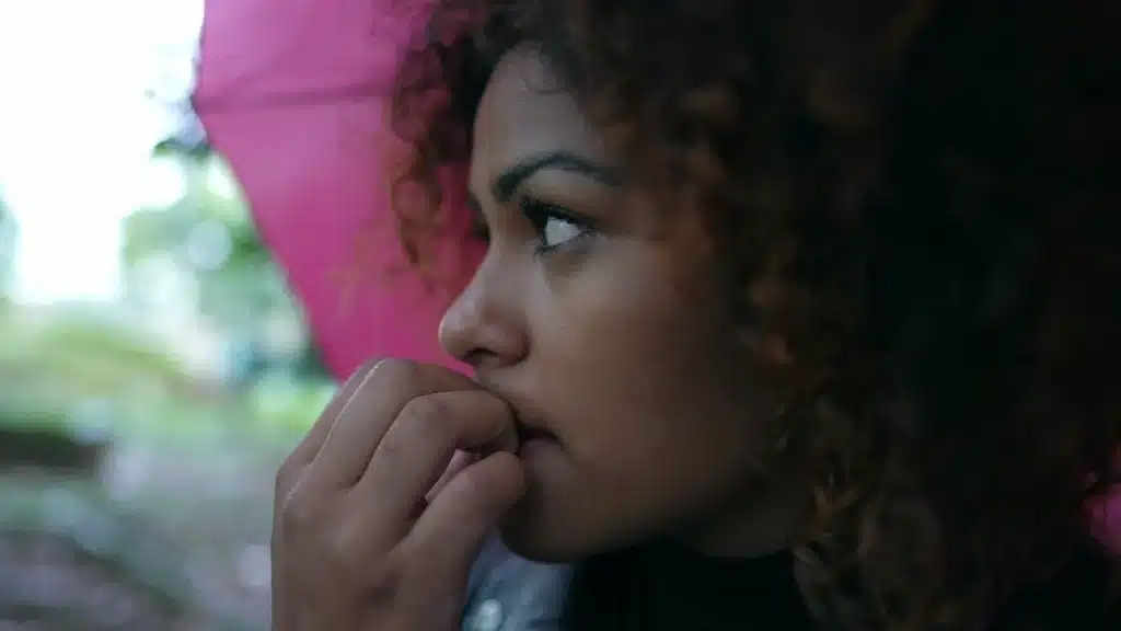 Woman looking thoughtful and anxious while sitting outside under an umbrella, reflecting on emotional recovery after trauma.