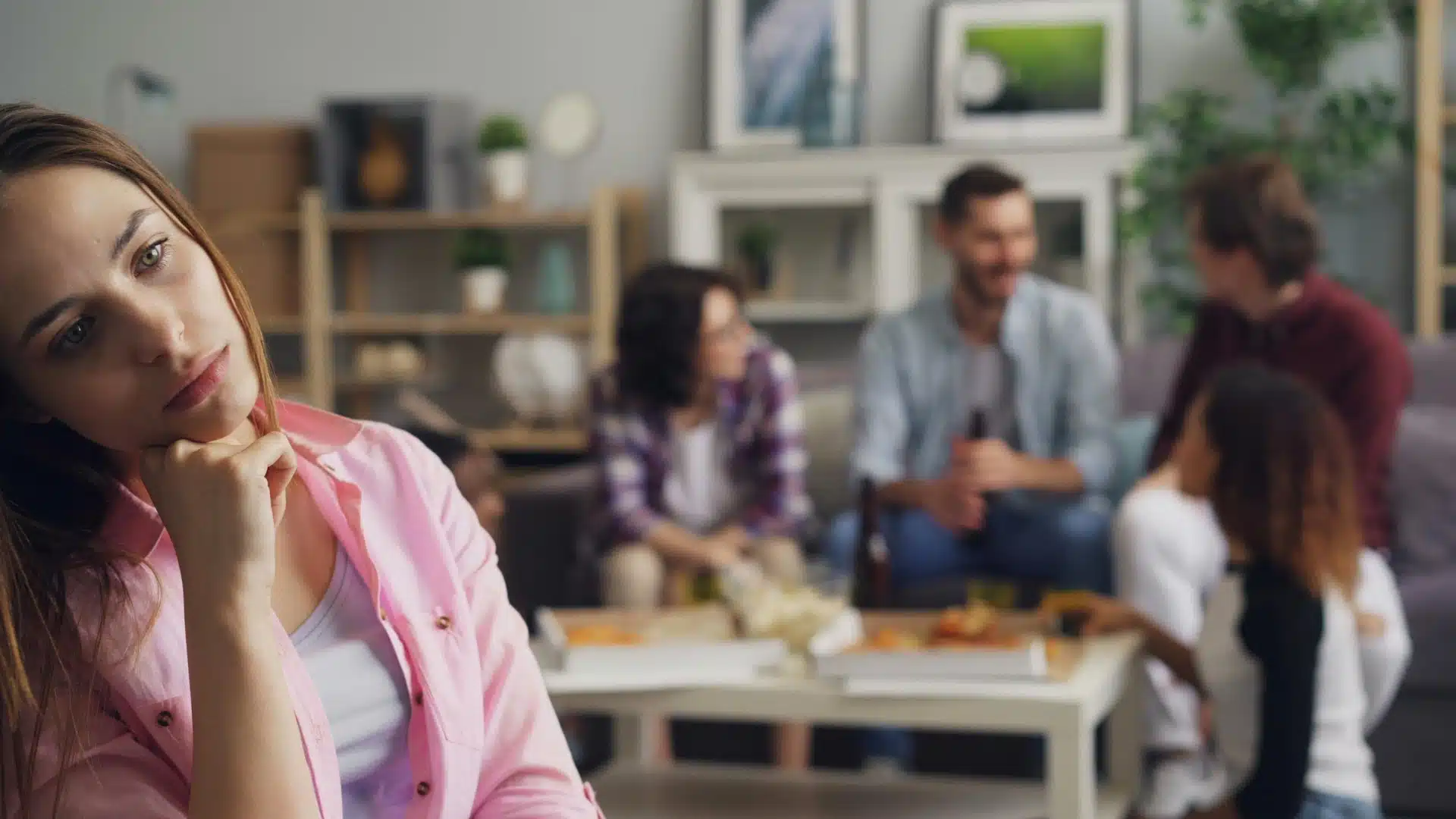 Woman sitting apart looking sad while friends talk in the background, symbolizing hidden depression and emotional isolation.
