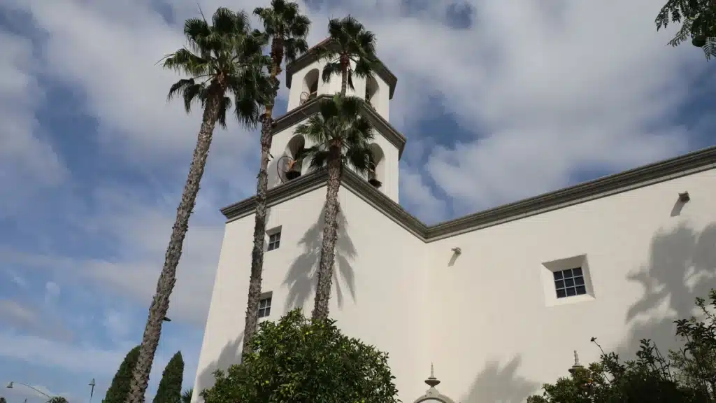 Mission San Juan Capistrano bell tower with palm trees against a blue sky in San Juan Capistrano, California