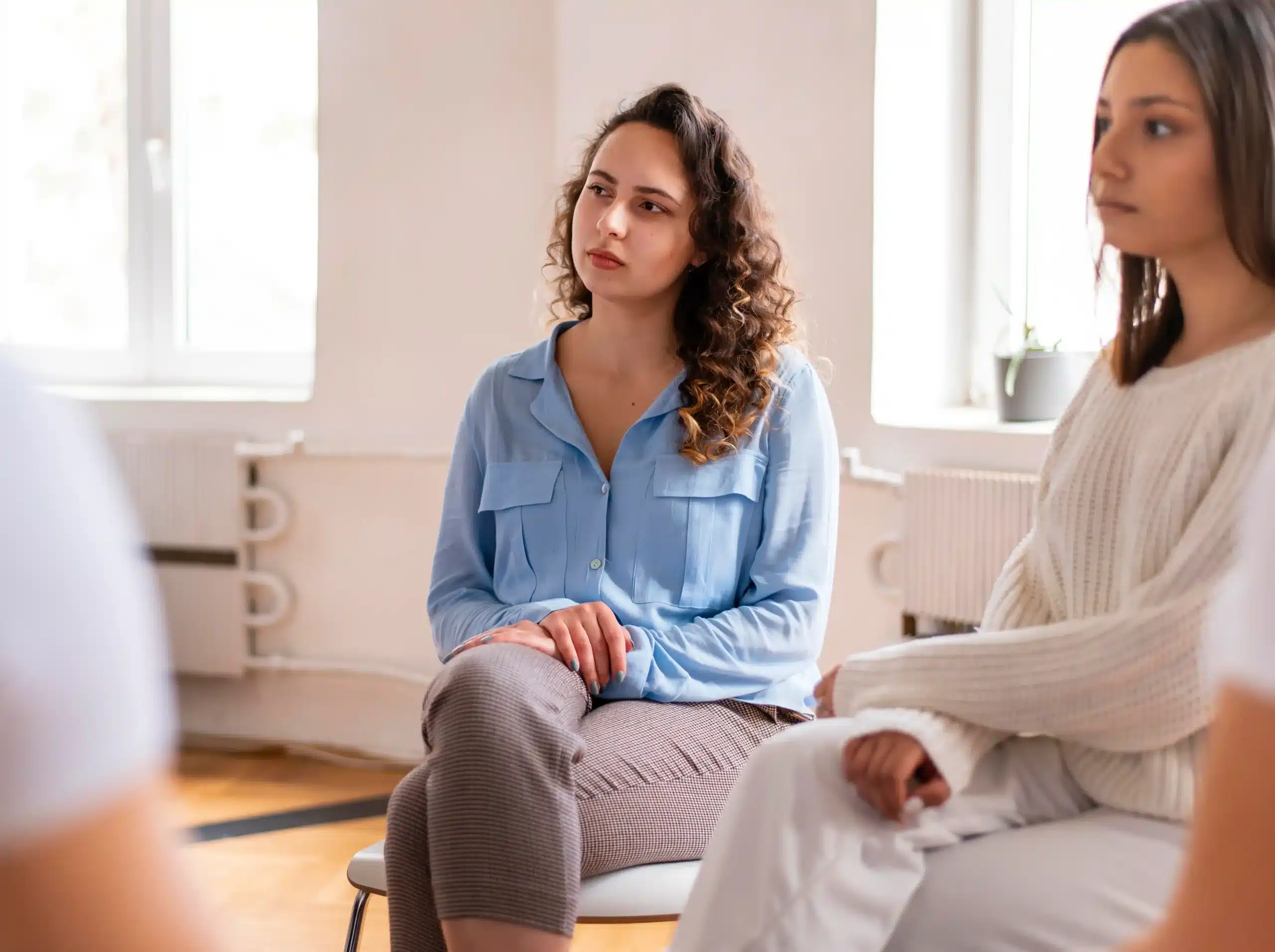 Two women seated in a bright room, attentively listening during a group discussion or support meeting.